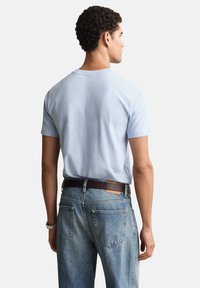 Svetlomodra bombažna majica s kratkimi rokavi, kombinirana z visokim pasom svetlo modrih jeansa in rjavim usnjenim pasom. Nežne šivske podrobnosti.