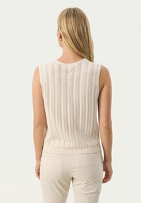 Gebreide mouwloze top in lichtbeige met verticale ribbelstructuur en contrasterende strak gebreide zoom. Heeft een ronde halslijn en een subtiele opening aan de achterkant.