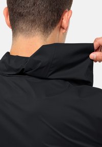 Giacca nera impermeabile con colletto alto. Il tessuto appare liscio e leggero, con un colletto regolabile per una vestibilità personalizzata. Nessun hardware visibile.