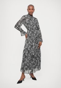 Μαύρο και άσπρο πασμίνα σχέδιο μακριά φόρεμα με μακριά μανίκια, σφιχτή μέση και φαρδιά φούστα. Συνδυασμένο με μαύρες γόβες.