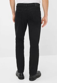 Jeans in denim nero con taglio dritto, dotati di due tasche posteriori e una vita visibile. Indossati con stivali neri.