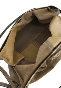 L'intérieur d'un sac à main en cuir brun et en daim présente une fermeture éclair, deux compartiments et un détail logo en ton doré. Texture douce et forme structurée.