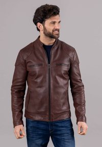 Brown leather jacket with quilted shoulder accents, zippered chest pockets, and a stand collar. Soft texture with a fitted design.
