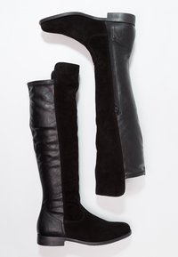 Botas negras hasta la rodilla que combinan cuero brillante y suave gamuza, con una cremallera lateral notable y suela de goma plana.