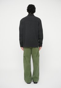 Svart mønstret skjorte med lange ermer, kombinert med løstsittende olivengrønne cargo-bukser, sett fra baksiden.