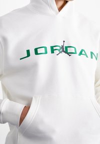Felpa bianca realizzata in tessuto morbido, con il logo verde "JORDAN" e una silhouette grigia di un giocatore di basket. Include una tasca frontale.
