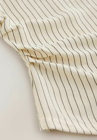 Gros plan d'un tissu beige avec de fines rayures noires verticales et une couture visible le long d'un pli.