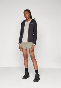 Black lightweight jacket with a hood, light grey T-shirt, and olive green shorts. Black hiking shoes with textured soles. Simple design elements.