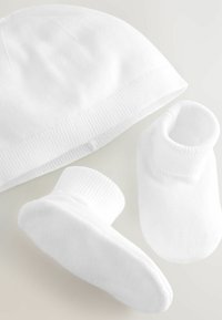 Bonnet en coton blanc avec un revers côtelé et des chaussons assortis en coton blanc, présentant une texture lisse et des formes arrondies.