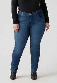 Skinny jeans in medium blue denim, featuring a high waist, front pockets, and minimal distressing. Paired with black ankle boots.