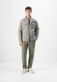 Gray quilted jacket with snap buttons and two chest pockets, paired with olive green pants and beige sneakers. Simple, functional design.