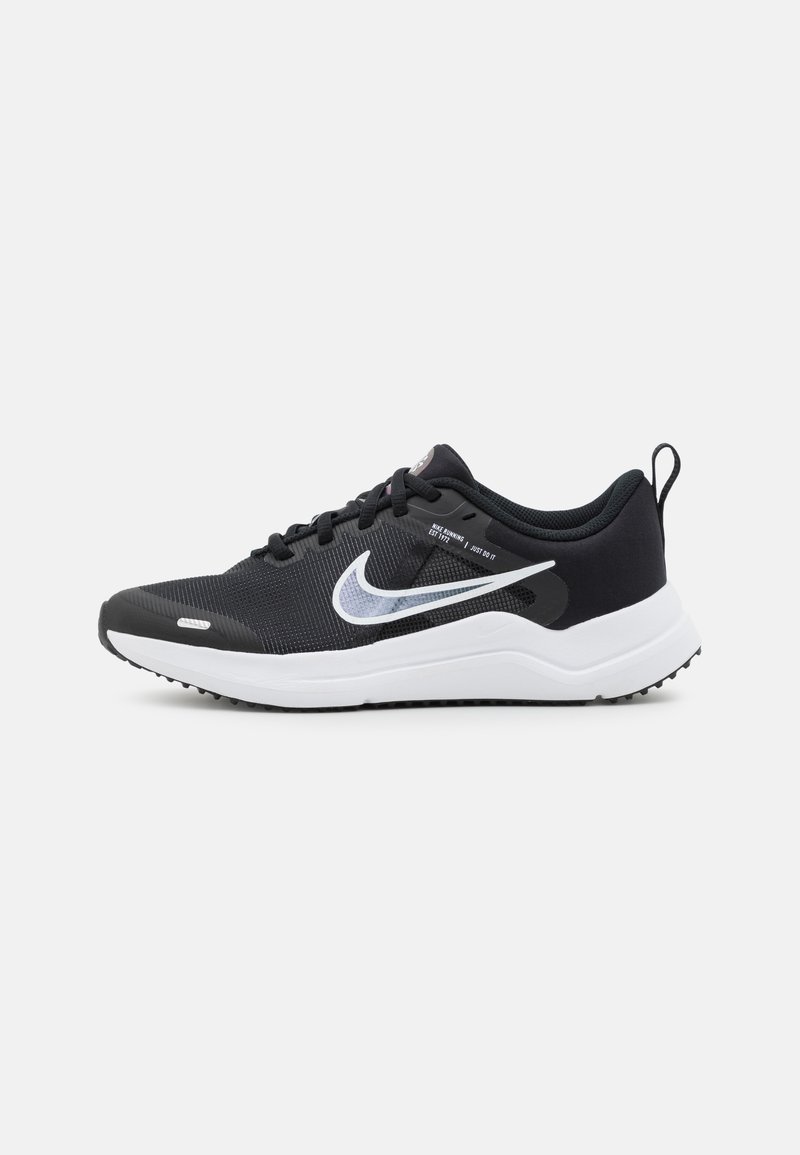 Chaussure de sport noire avec une tige en mesh texturé, semelle intermédiaire blanche et semelle en caoutchouc. Dispose de lacets noirs et d'un logo swoosh blanc bien visible.