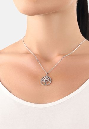 Collana d'argento con un pendente rotondo ad alberello della vita indossata al collo di una donna, abbinata a una maglietta bianca a scollo rotondo.