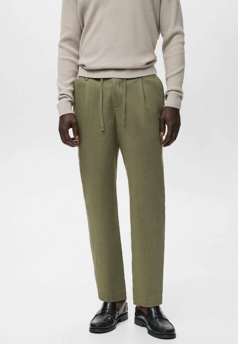 Pantalones verde olivo con pliegues, cintura con cordón y corte a la altura del tobillo. Combinados con un suéter beige de canalé y zapatos negros.