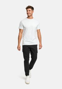T-shirt bianco a maniche corte abbinato a pantaloni cargo neri e sneakers bianche. L'outfit presenta una vestibilità casual e rilassata con un tessuto resistente.