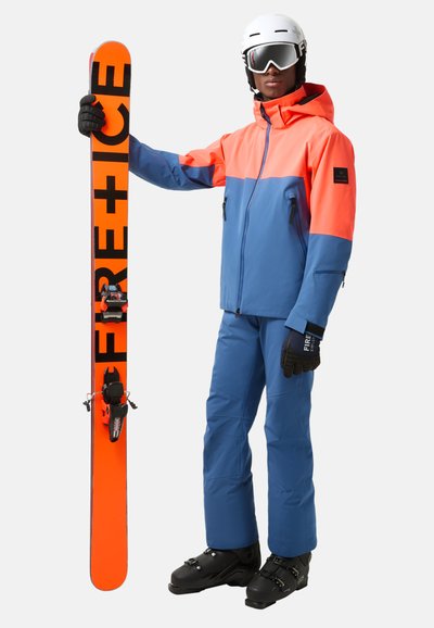 Sprzęt narciarski obejmuje niebieską i pomarańczową kurtkę z kapturem, pasujące niebieskie spodnie, czarne rękawice oraz pomarańczową deskę narciarską z czarnym napisem.