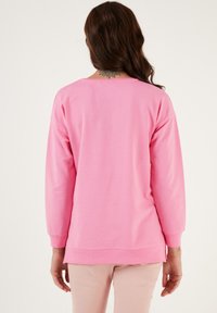 Felpa a maniche lunghe in cotone rosa brillante. Caratterizzata da una scollatura ampia e polsini a costine. Tessuto morbido con una vestibilità rilassata e aperture sottili sull'orlo.