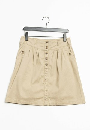 Jupe en coton beige khaki avec une silhouette évasée, dotée d'une fermeture à boutons sur le devant, de poches latérales et de plis subtils. Accrochée à un crochet noir.