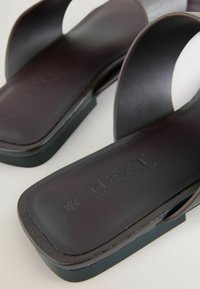 Sandales slide noires à bout carré avec larges brides et marquage « NEXI » embossé sur la semelle intérieure rembourrée.