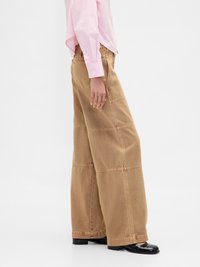 Lys brun vide benbukser laget av denim, med synlig søm og glidelåslukking, sammen med en rosa stripete skjorte.