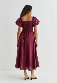 Burgundia midi kleit puffvarrukatega, smock-tüüpi bodi ja voolava kangaga. Omab laia lõiget ja alläänt, mis ulatub põlvedest allapoole.