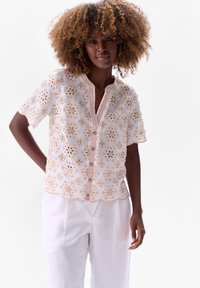 Witte blouse met geborduurde beige bloemen, korte mouwen, een gegolfde zoom en een knoopsluiting aan de voorkant met een zachtroze bies.