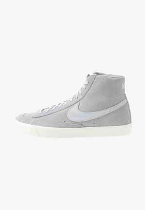 Zapatilla Nike de ante gris de caña alta con logotipo de swoosh blanco, cordones blancos y suela de goma blanca, aislada sobre un fondo blanco.