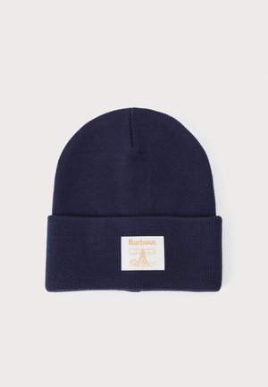 Beanie lavorata a maglia blu navy con orlo ripiegato. Presenta un'etichetta quadrata crema con un design e testo arancione. Texture morbida e forma cilindrica.