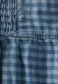 Sininen denimi, jossa on ruutukuvio, kerätty rakenne ja vastakkaiset kiinteät osat. Ompeleet näkyvät selvästi.