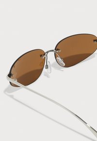 Sunglasses s bronzovým nádechem, oválný tvar, kovový rám ve stříbrné, tenké nožičky a průhledné nosní polštářky pro pohodlí.