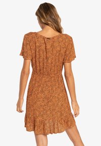 Robe orange à manches courtes avec une taille cintrée, un ourlet à volants et un motif léopard noir. Fabriquée en tissu léger.