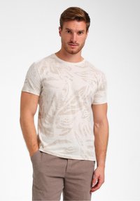 T-shirt beige clair avec un motif de feuilles, fabriqué en tissu doux, avec un col rond et des manches courtes. Associé à un pantalon texturé.