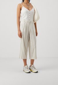 Vit knäppt linne med tunna axelremmar, tillsammans med beige och vita horisontellt randiga vida byxor och chunky sneakers.