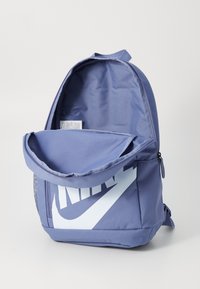 Lila szövet hátizsák nagy fehér Nike logóval. Zipperes fő rekesszel és felső fogantyúval rendelkezik, texturált külső résszel.
