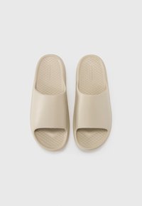 Sandales à glisser beige en caoutchouc lisse, avec un bout ouvert, une large sangle et une semelle intérieure texturée avec un motif en diamant pour l'adhérence.