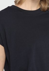 Černé bavlněné tričko s kulatým výstřihem a krátkými rukávy. Tkanina se zdá být měkká s hladkým povrchem a designem uvolněného střihu.