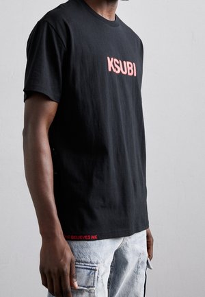 Schwarzes Baumwoll-T-Shirt mit pinkem "KSUBI"-Logo auf der Vorderseite und rotem Text "SOME BELIEVES ME" am Saum. Klassische Passform mit Rundhalsausschnitt.