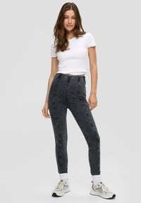 Czarne legginsy elastyczne z teksturowanej tkaniny, z elastycznym paskiem w talii i bocznymi szwami, w połączeniu z dopasowaną białą koszulką i trampkami.