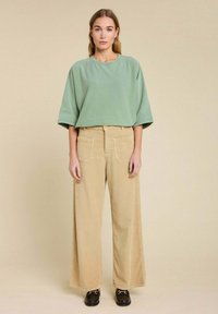 Un haut ample vert menthe à manches courtes associé �à un pantalon en velours côtelé large beige avec de grandes poches arrière et des chaussures noires à lacets.