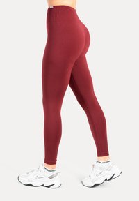 Leggings bordeaux à taille haute, fabriqués en tissu stretch. Portés avec des baskets blanches ornées d'accents argentés et une chaussette à motifs.