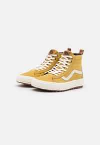 Sneaker alte in suede giallo senape, con lacci bianchi, una striscia laterale bianca e una patch con logo marrone sulla linguetta.