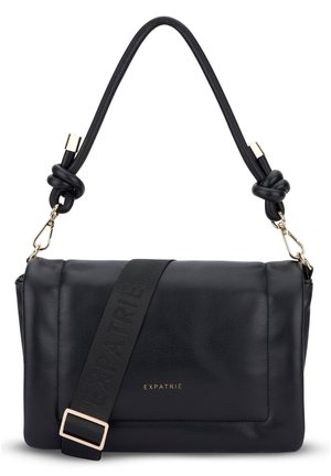 Sac à bandoulière en cuir noir avec poignée nouée, bandoulière large amovible et nom de marque doré "EXPATRIÉ" sur le rabat avant.