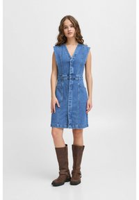 Denim haljina svijetloplave boje, s V-izrezom, bez rukava, elastičnim strukom, prednjim džepovima i dužinom do koljena. Nosi se s smešnim čizmama do koljena.