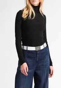 Black long-sleeve turtleneck top paired with high-waisted blue denim jeans. White belt with a silver buckle featuring the brand name.