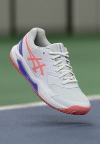 Sport-Schuh mit einem oberteil aus hellgrauem Mesh, pinken und lila Akzenten, einer Gummisohle mit strukturiertem Grip und verstärktem Zehenschutz.
