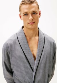 Albornoz a rayas gris con ribete negro a lo largo del cuello. Hecho de tela suave, cuenta con un logo en el pecho y un ajuste relajado.