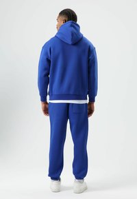 Blue hoodie with a large hood, kangaroo pocket, and ribbed cuffs, paired with matching joggers featuring elastic cuffs and a back pocket.