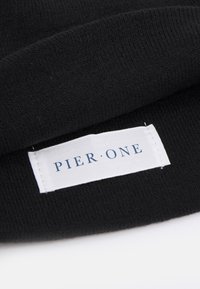 Black knitted beanie with a textured surface, featuring a sewn white label that reads "PIER ONE" in navy blue text.