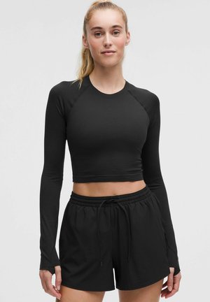 Czarny krótki top z długim rękawem o prążkowanej fakturze i otworami na kciuki, zestawiony z czarnymi szortami na sznurku. Prosty design, bez wzorów i akcentów.