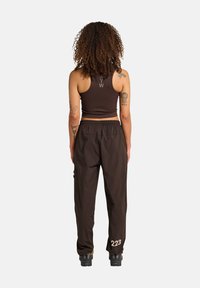 Brun, cropped tank top med lys tekst; parret med løst siddende joggers i brun farve med sidelommer og hvid "223" på det højre ben.